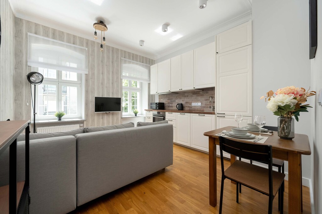 A wide view of the living area and kitchen with elegant lighting, a small dining table, and light wood flooring enhancing the spaciousness.