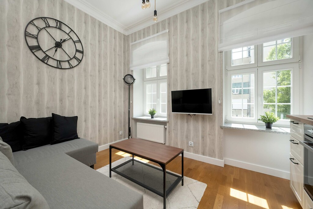 Another angle of the living area with a sectional sofa and wall-mounted TV, highlighting the bright ambiance from the natural daylight.