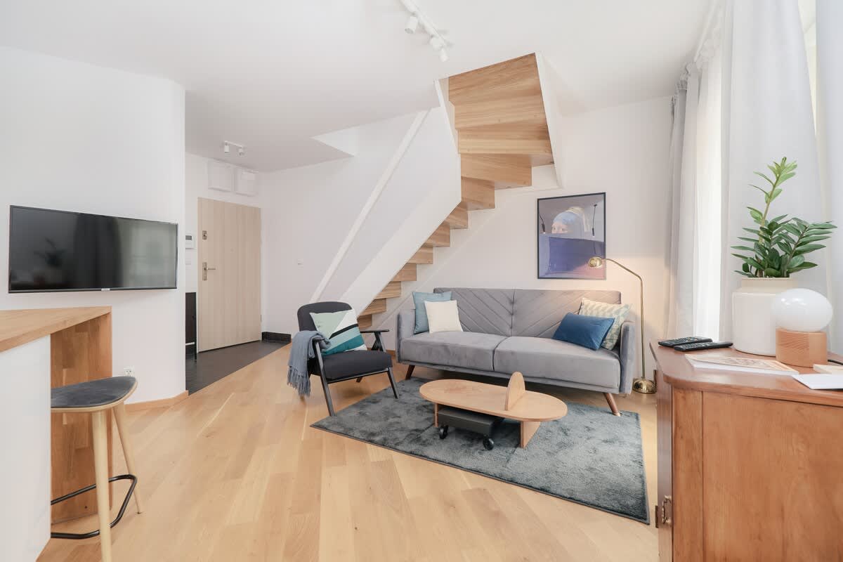 A bright living room with a sloped ceiling, modern furniture, and a flat-screen TV on a wooden stand.