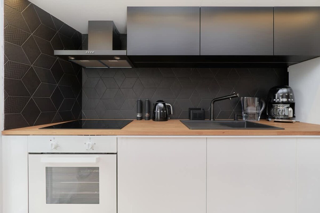 A modern kitchen featuring white cabinets, a black backsplash, and built-in appliances like a oven.
