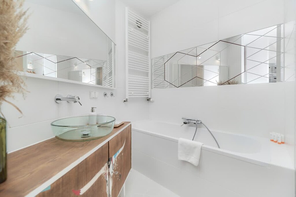 A sleek bathroom with white tiles, a bathtub, and a wooden countertop with a sink.