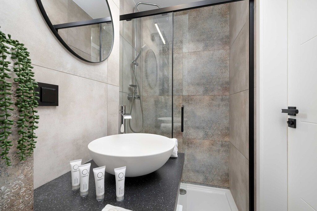 A stylish bathroom with a walk-in shower and rainfall showerhead. Stone-like tiles and greenery create a spa-like atmosphere.