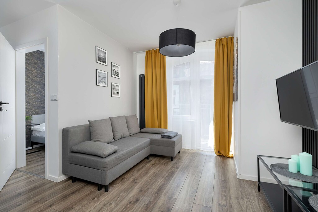 A bright living space with a gray sofa bed and yellow curtains. The setup offers both a place to relax and an extra sleeping area.
