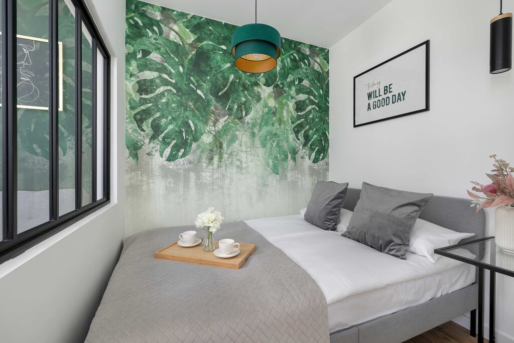 A peaceful bedroom featuring a comfortable bed, green accent walls, and large leafy prints. Perfect for rest and relaxation.