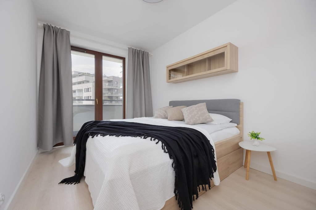 A bright bedroom featuring a double bed with minimalist decor and access to a balcony through large glass doors.