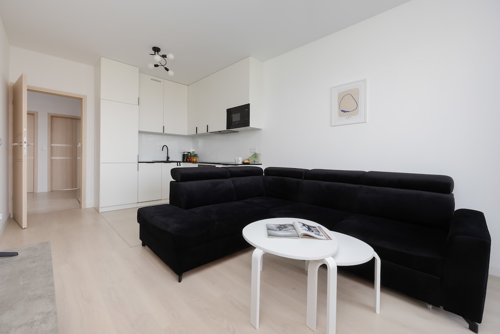A spacious open-plan living room with sleek black and white furnishings and a mounted television.

