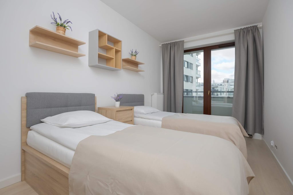 A second bedroom arranged with two single beds, modern shelving, and a soft color palette.

