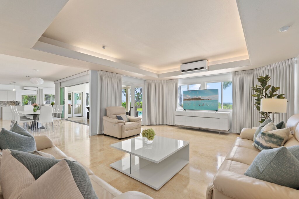 Natural light fills the plush living room, where floor-to-ceiling glass connects indoor comfort to tropical serenity beyond.