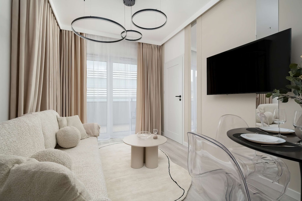 Bright and cozy living room with beige sofa, TV, round table and access to balcony.