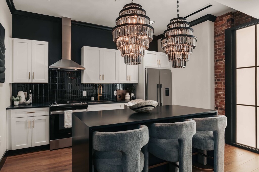 The modern kitchen features smoky accents and mirrored finishes, highlighted by stunning glass chandeliers and comfortable bar stools at the island—blending style and function effortlessly.