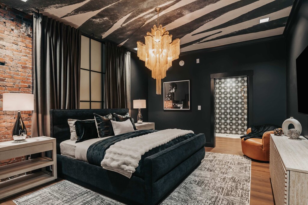 The large king bed is accented with rich velvets and layered textures, complemented by bold design details—including striking wallpaper on the ceiling.