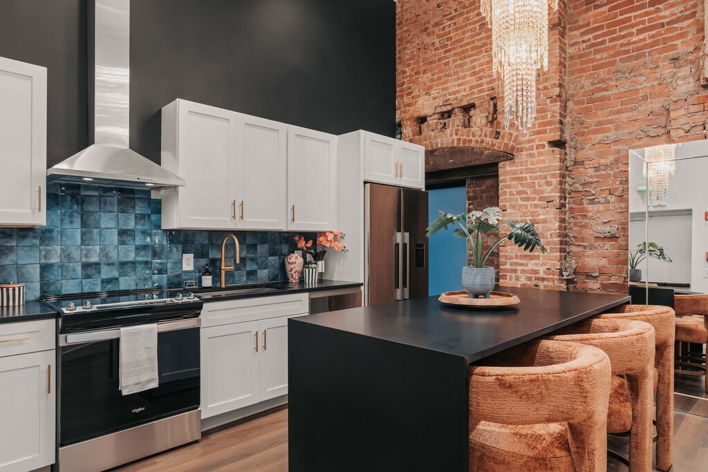 The fully stocked kitchen features a stunning chandelier, state-of-the-art appliances, and a sleek island with three plush, upholstered seats—perfect for casual dining or morning coffee.