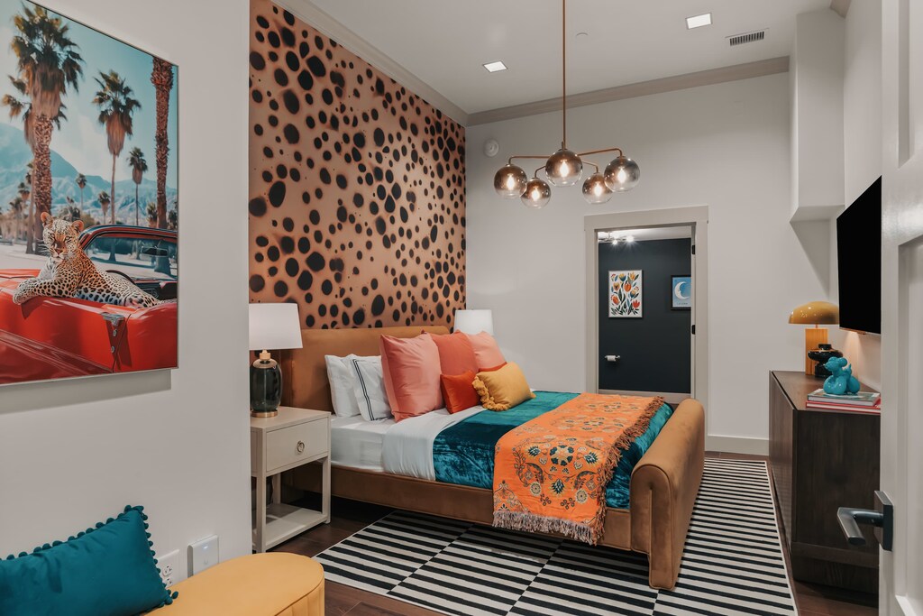 This king bedroom makes a bold statement with vibrant cheetah-print wallpaper, rich textures, and bright, playful hues—balanced by a sleek smart TV for modern comfort.