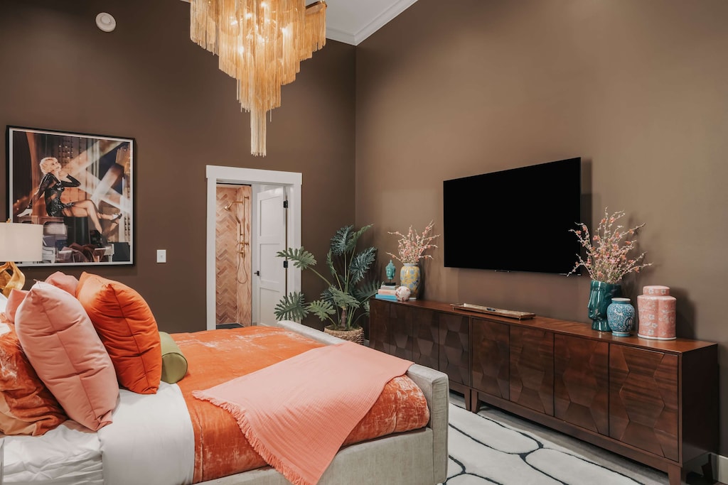 The master bedroom showcases a plush king bed, an elegant chandelier, refined decor, and a smart TV. 