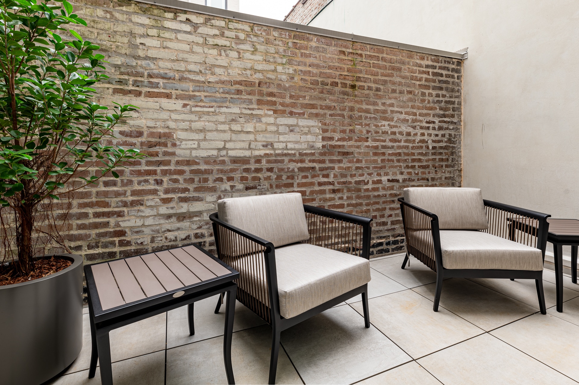 Private outdoor patio featuring modern lounge chairs, side tables, and a rustic exposed brick wall.
