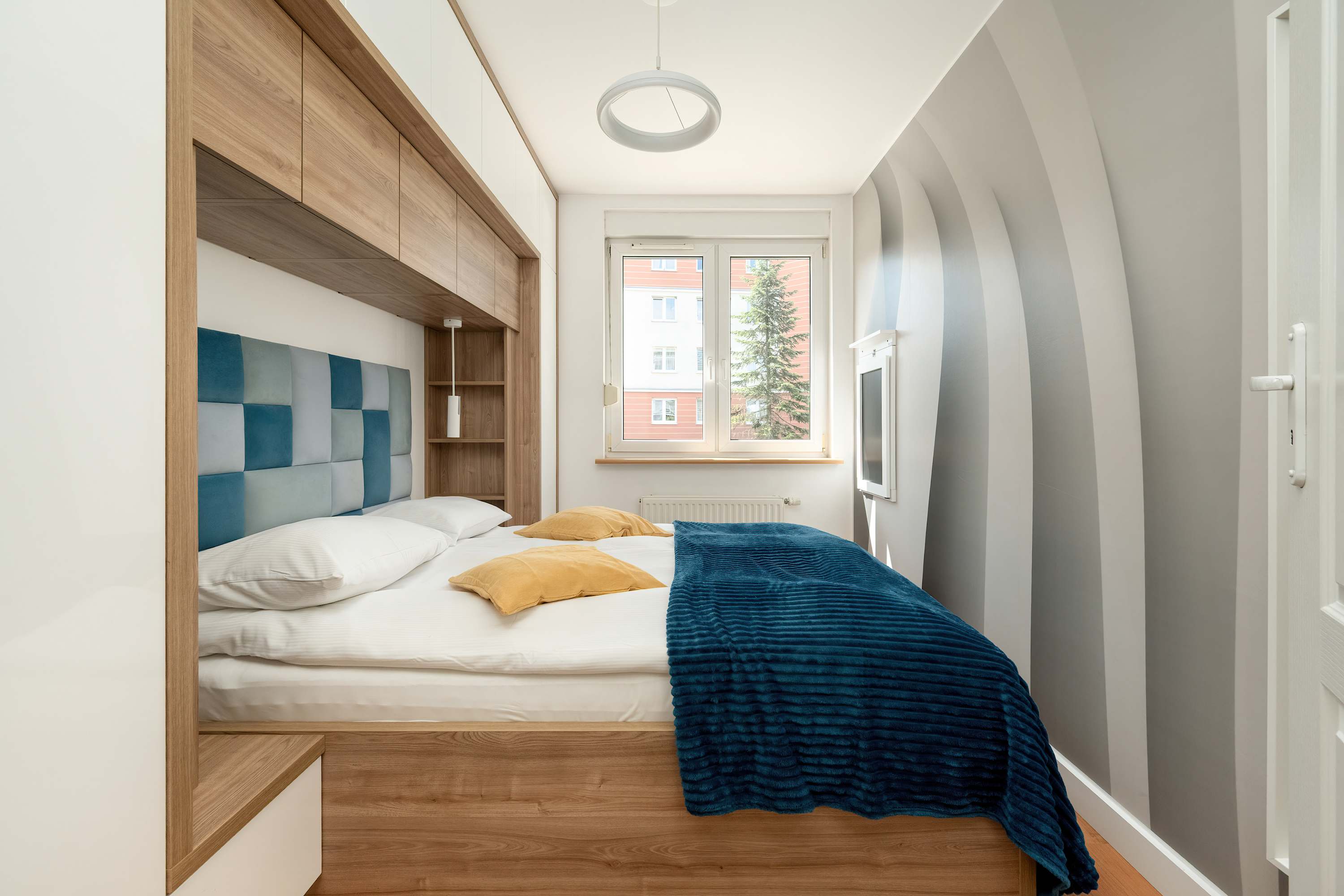 The second bedroom with a padded headboard and large window is a peaceful oasis after a busy day.