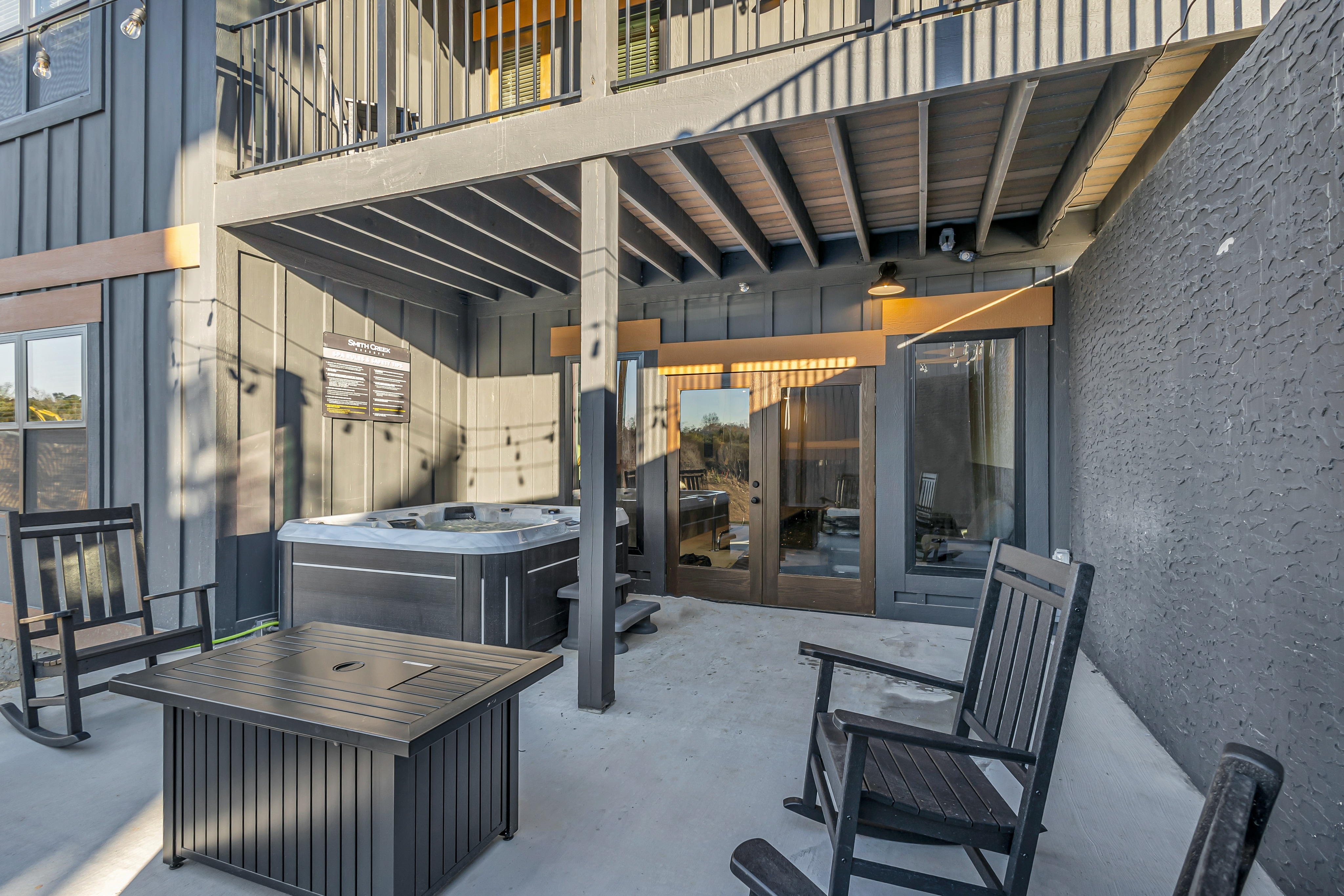 A relaxing patio space featuring a luxurious hot tub, comfortable rocking chairs, and a fire pit for cozy evenings.