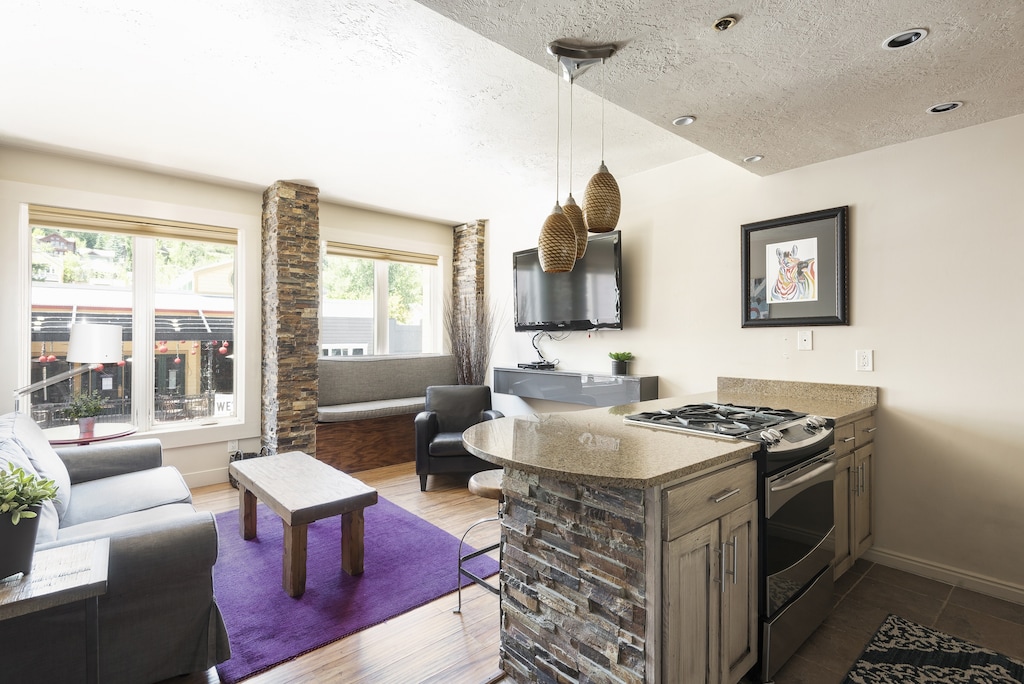 Kitchen breakfast bar and oven/range with granite countertops, living room in the background with bright purple area rug for a beautiful pop of color
