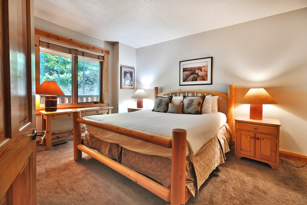 Second bedroom with wooden bedframe, king bed, large picture window with mountainside views