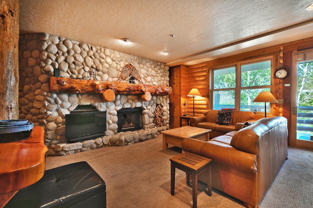 River rock fireplace with feature single log mantle, flat screen TV, full couch and love seat