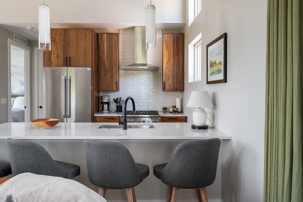 - Sleek kitchen with stainless steel fridge and stove   - Modern island with bar seating and pendant lighting   - Bright windows bring in natural mountain light