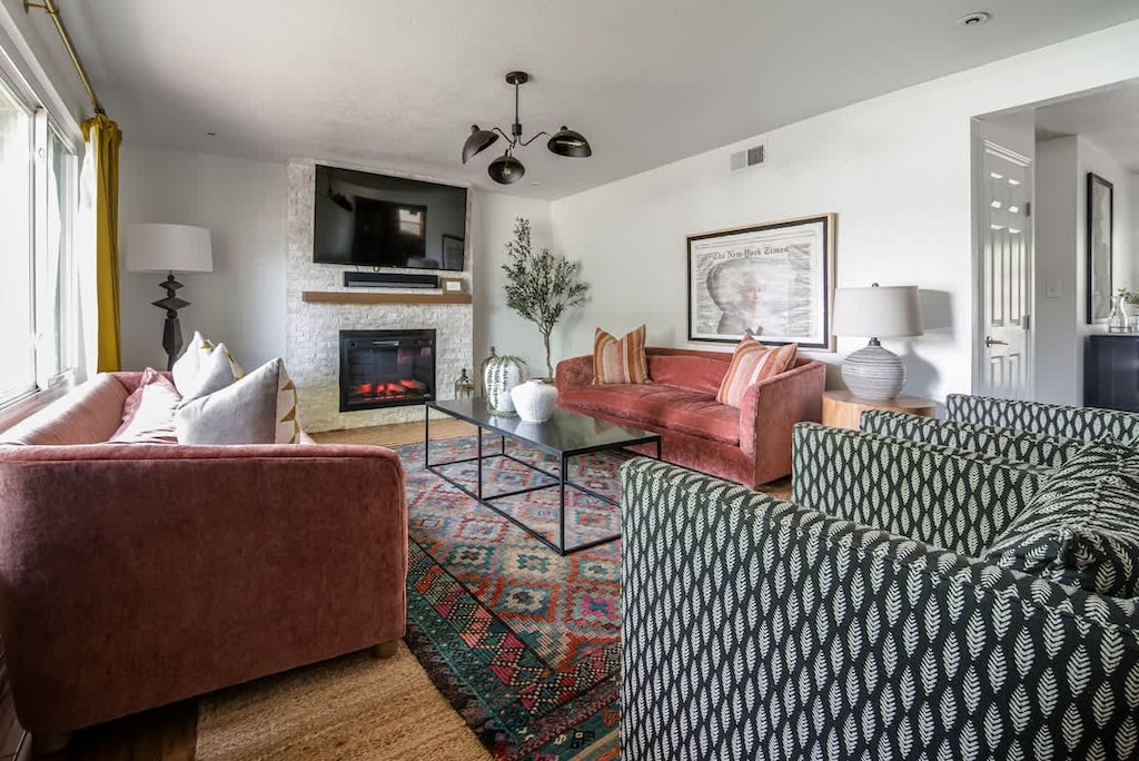 A cozy living room featuring a sleek flat screen TV, two coral velvet couches, and two stylish black and white accent chairs. The space exudes warmth with cozy touches throughout.