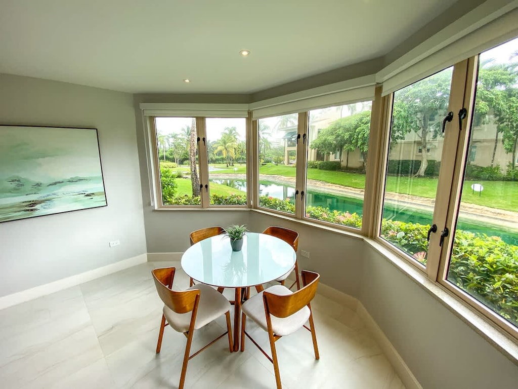Breakfast nook, with panorama windows, overlooks landscaped gardens with a hint of ocean views; seats 4 on padded chairs around a circular dining table.