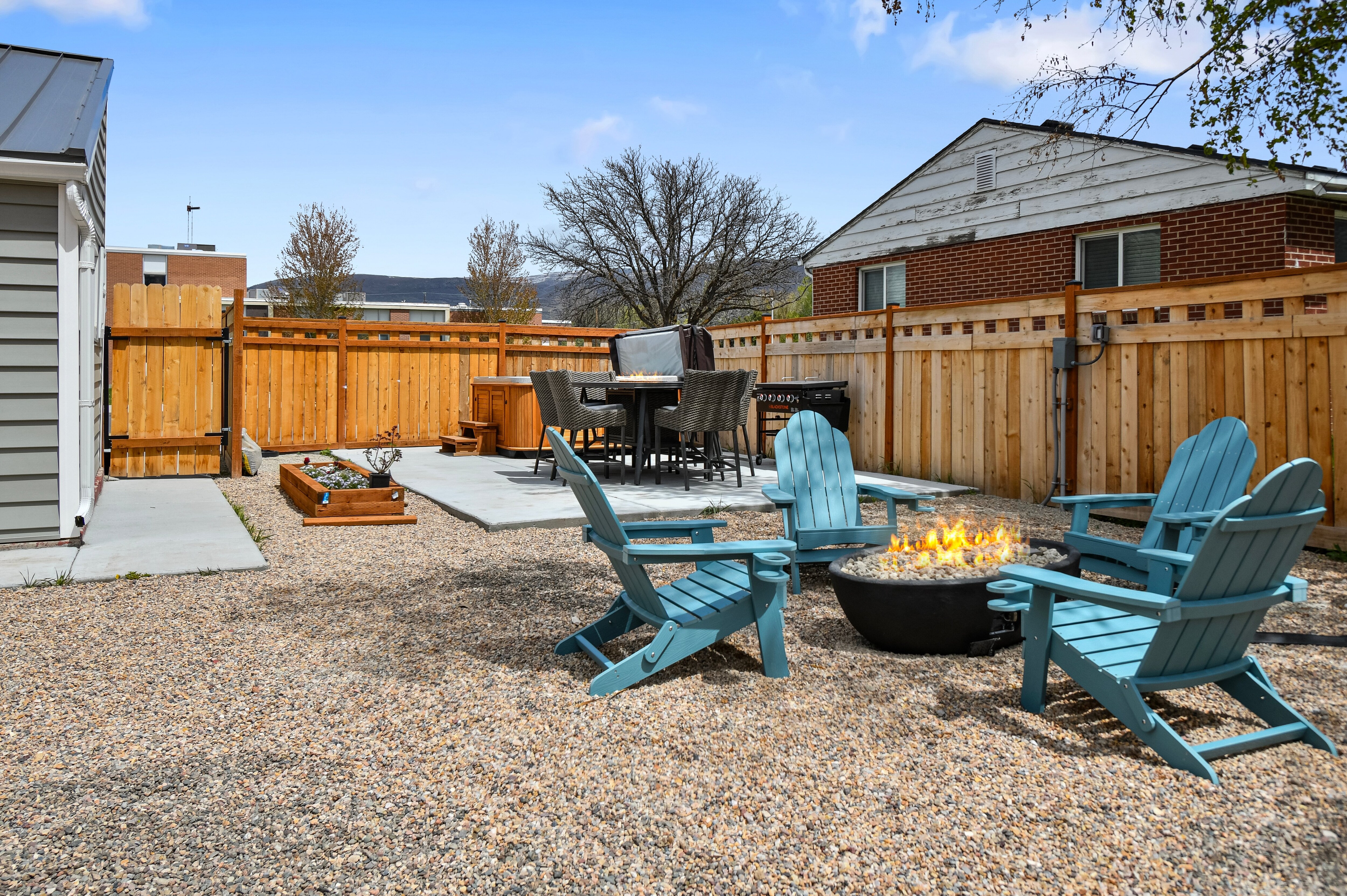 The large backyard is fully landscaped with Firepit, Adirondack Chairs, Hot Tub, Blackstone BBQ Grill, and Outdoor Dining table