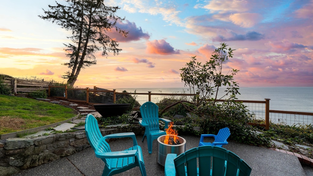 Oceanfront patio with chairs and firepit at sunset.