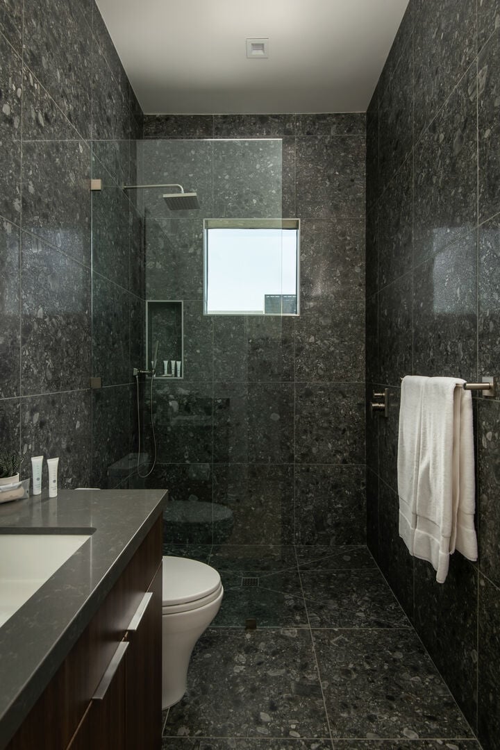 The spacious, modern walk-in shower, complete with a rain shower head, textured stone tile, and a clerestory window for natural light.