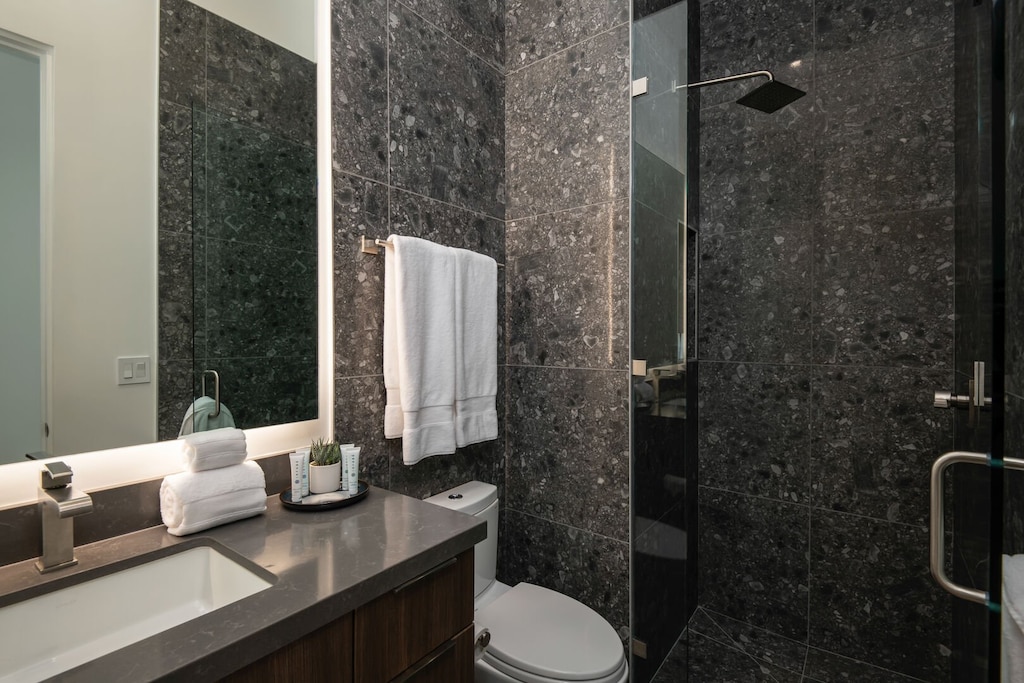Step into the stunning guest bathroom with floor-to-ceiling dark stone tile and a sleek glass-enclosed shower.