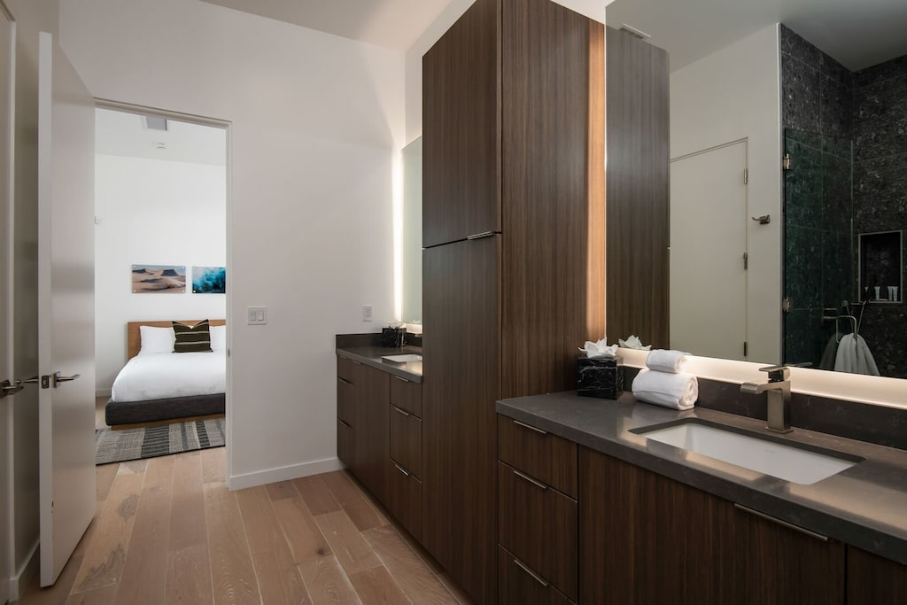 The well-appointed guest bathroom vanity, showcasing excellent storage and high-end fixtures, offering a glimpse into the adjacent bedroom.