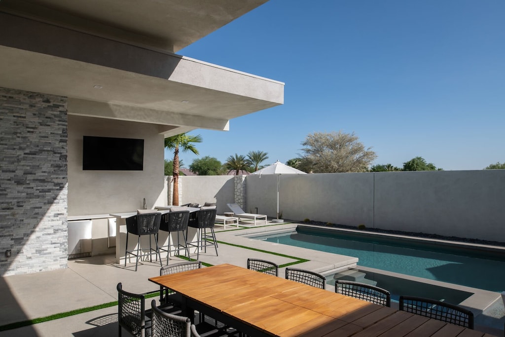 Your daytime paradise! The covered patio features a dining table for 8, bar seating, a wet bar, and an outdoor TV for year-round enjoyment.