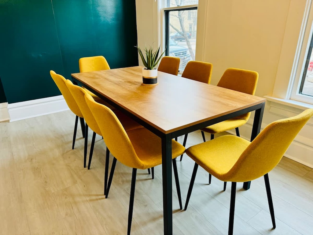 Host memorable gatherings in our stylish dining area at Jungle House Airbnb, featuring a sleek wooden table, vibrant yellow chairs, and a lush green accent wall  The perfect blend of modern elegance and cozy charm in Short North Columbus