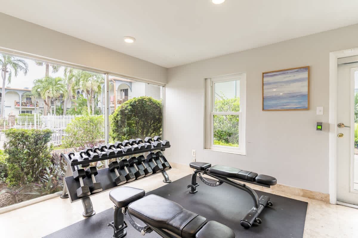 Bright fitness space with adjustable benches and a full set of dumbbells, overlooking lush landscaping