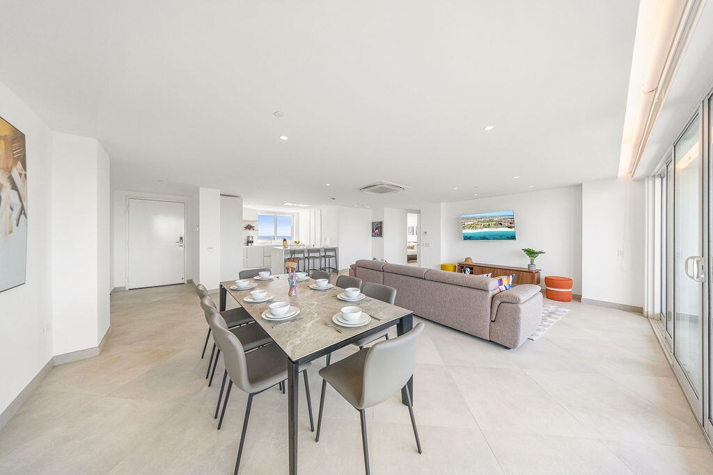 Step into this bright, open-plan living space where your group can gather around the dining table for meals or relax on the plush sofa together. Floor-to-ceiling windows bathe the room in natural light and invite coastal breezes in.