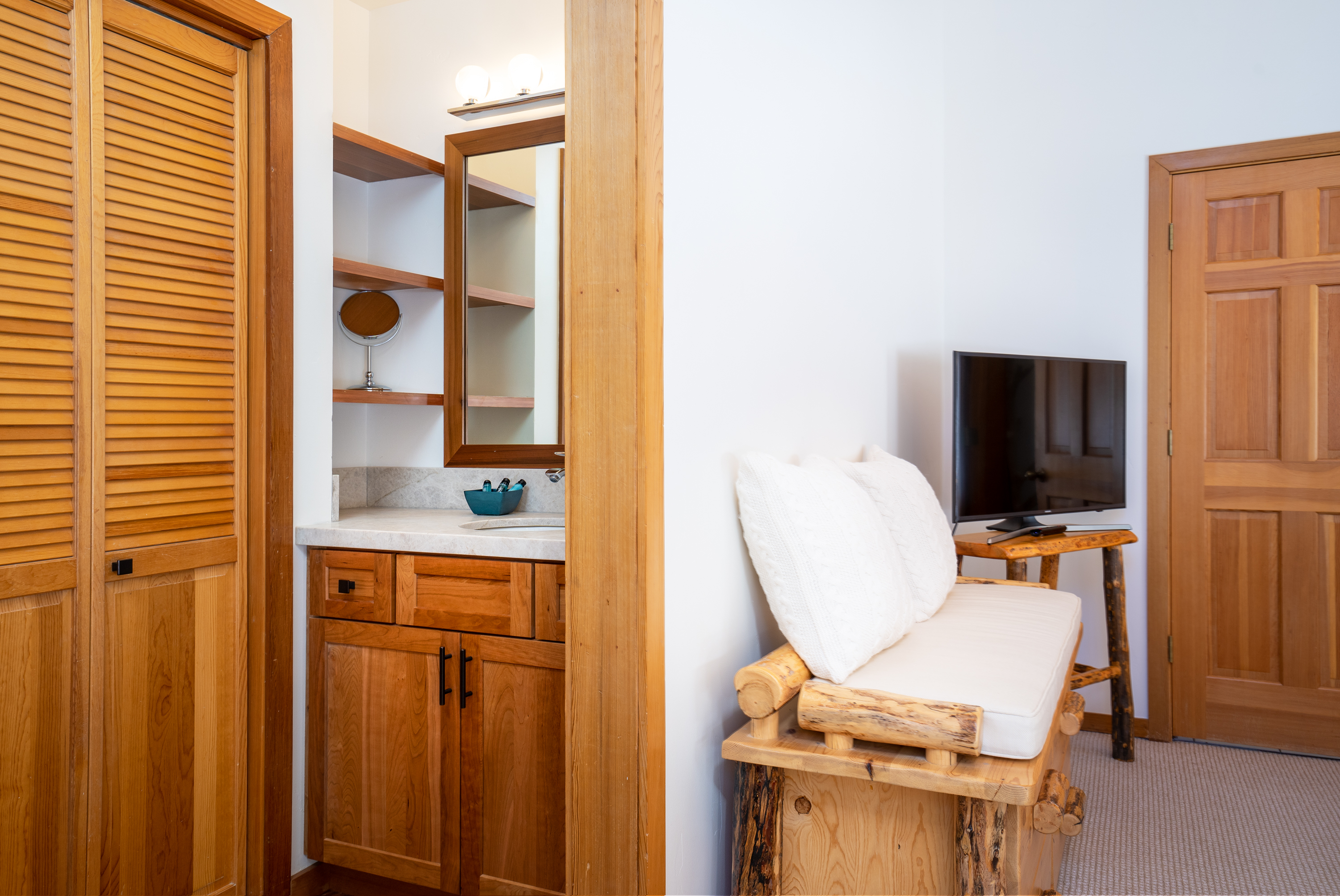 Showing a cushion log bench seating w/storage drawers, flat-screen TV, single vanity w/natural stone counter and shelves, cherry wood cabinet, large closet