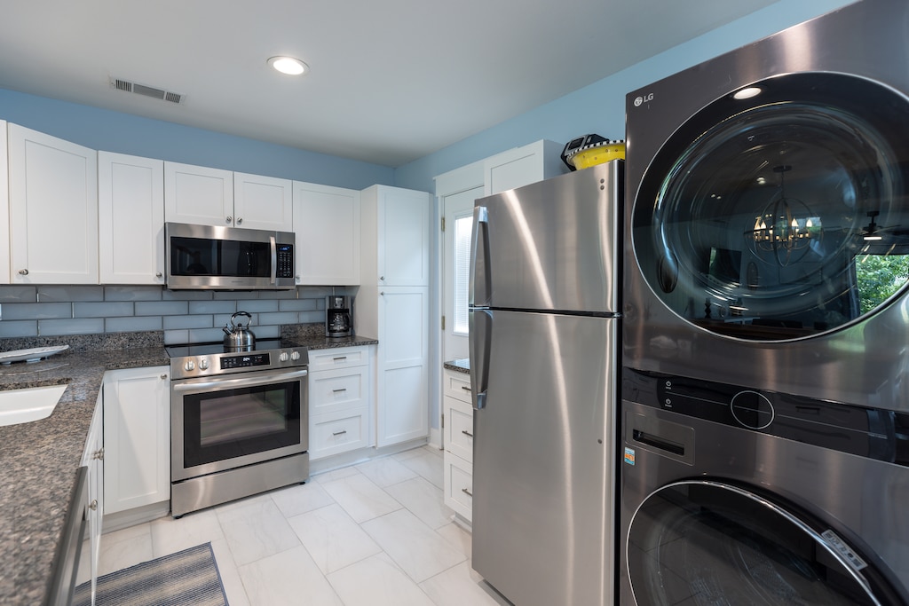 Modern kitchen with stainless steel appliances and white cabinetry with a washer and dryer