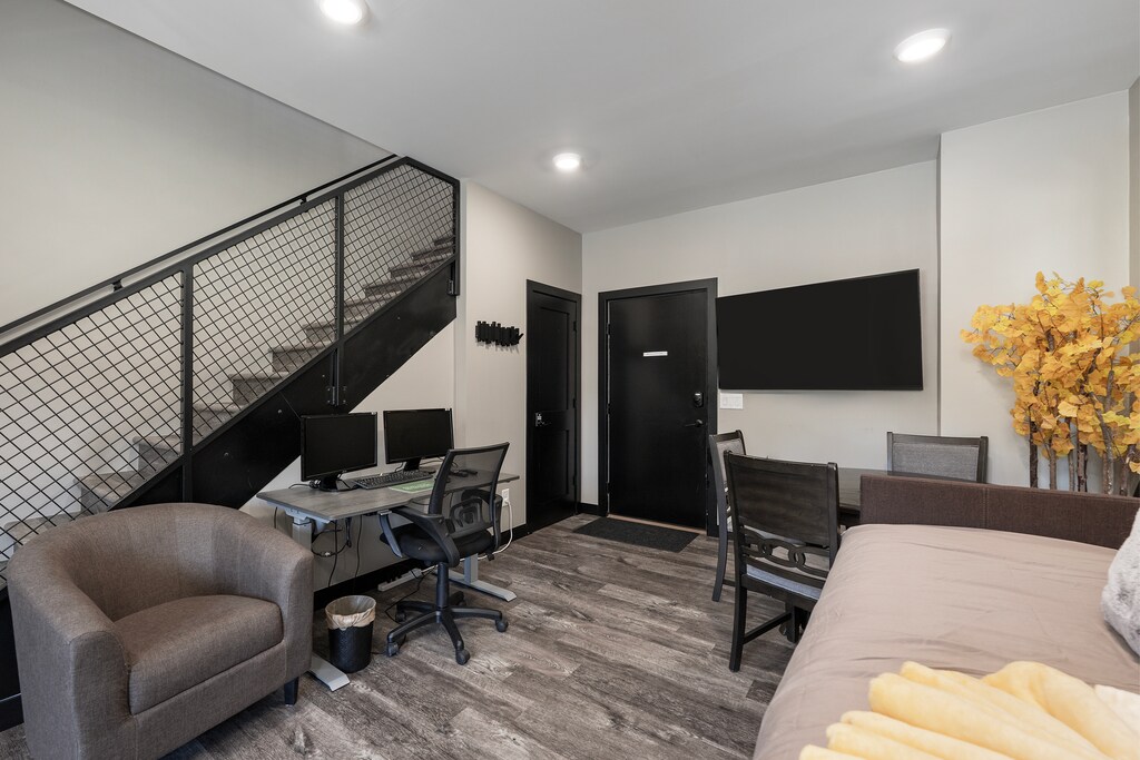 Your spacious living area blends modern comfort with industrial style, featuring a cozy workspace and entertainment zone beneath striking architectural stairs.