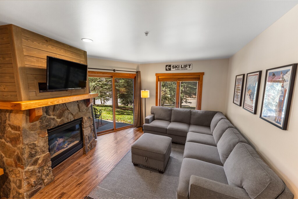 Living area with cozy sectional, gas fireplace w/ stone surround, mounted flatscreen TV and access to the private balcony. 
