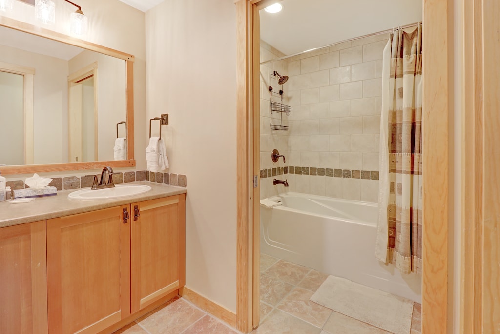 Warm and inviting bathroom featuring a double-sink vanity and a tiled tub/shower combination. Ideal for relaxing after a day of mountain activities.