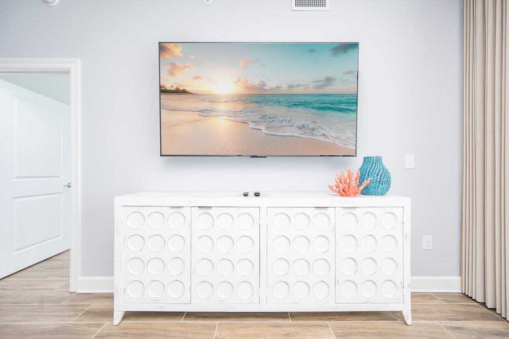 Enjoy the large TV above a stylish white cabinet, complemented by colorful decor and inviting textures in the living area