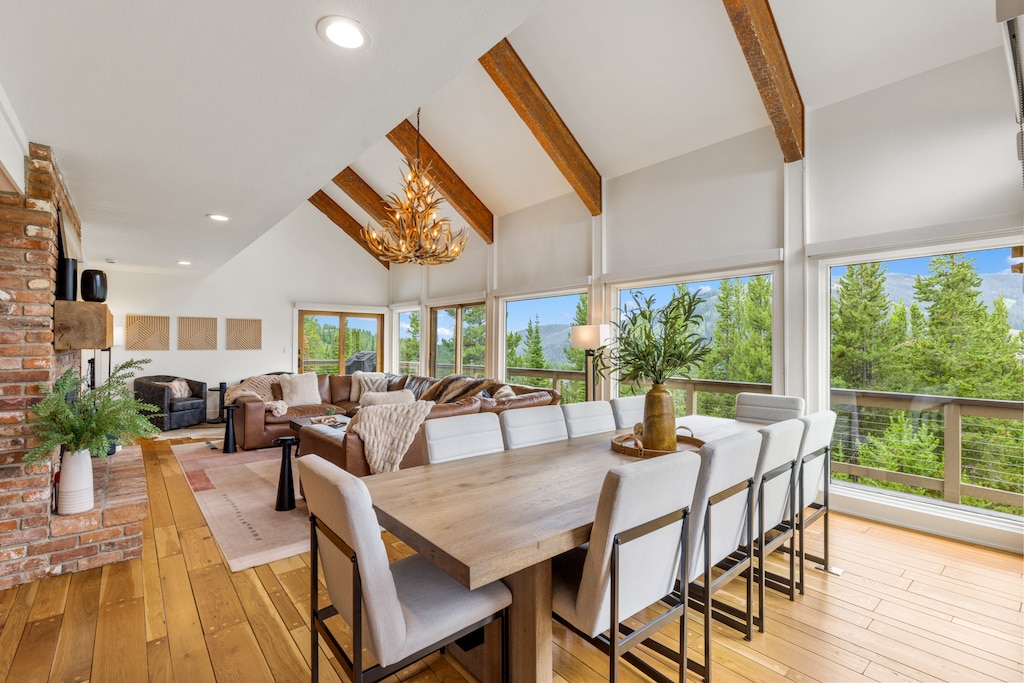 Gather around the stunning dining table beneath soaring beamed ceilings with breathtaking mountain views. The open layout flows seamlessly to a cozy living area with a warm fireplace.