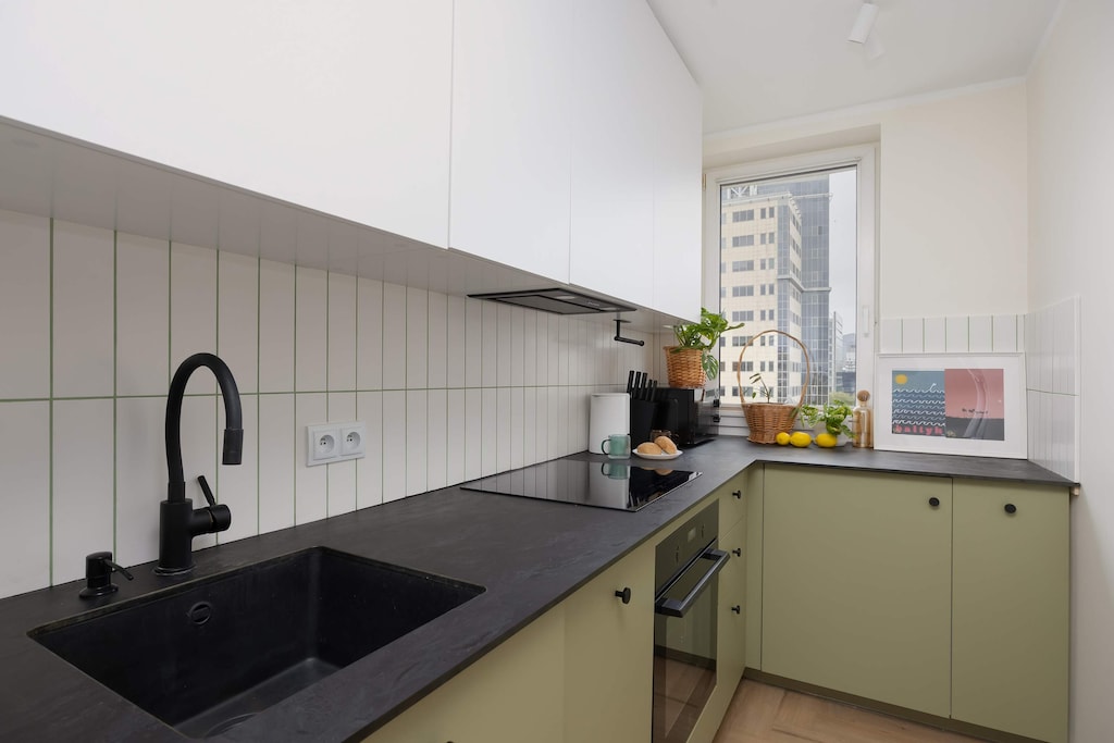 A stylish modern kitchen with green cabinets, a black countertop, and sleek built-in appliances.
