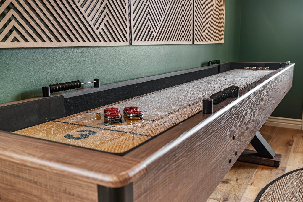 A large media room with desk, smart TV, shuffle board and sleeper sofa