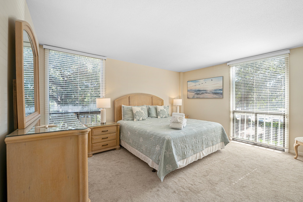 A serene primary bedroom filled with natural light, featuring a king bed with coastal-inspired bedding and soothing neutral tones.