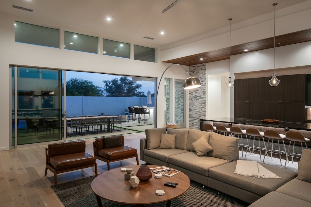 The grand living space seamlessly opens to the patio with disappearing glass doors, blending sophisticated indoor comfort with the vibrant outdoor scene at twilight.