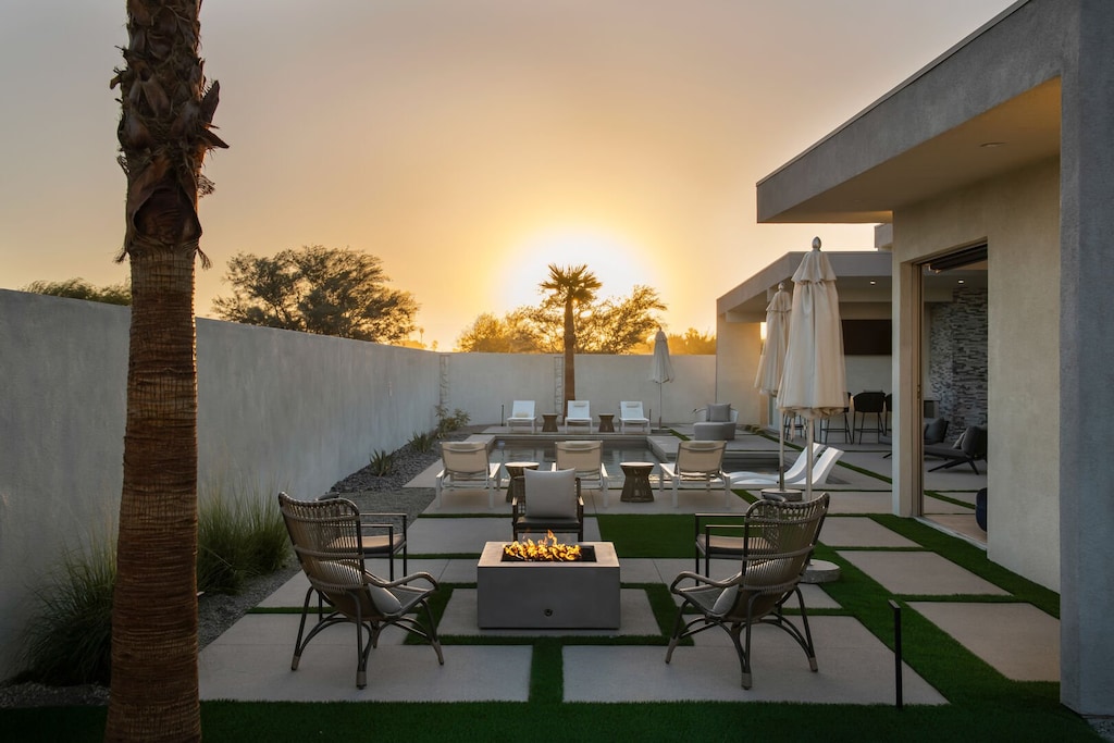 Catch a beautiful desert sunset from the cozy outdoor fire pit lounge area, framed by palm trees and soft light.