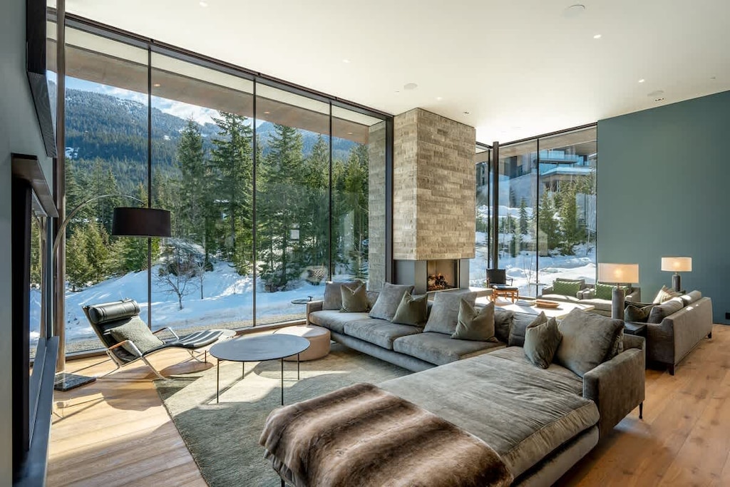 - Expansive living area with panoramic mountain views  
- Plush seating by the fireplace creating a warm mountain vibe  
- Natural light fills the space with a serene snowy backdrop  
