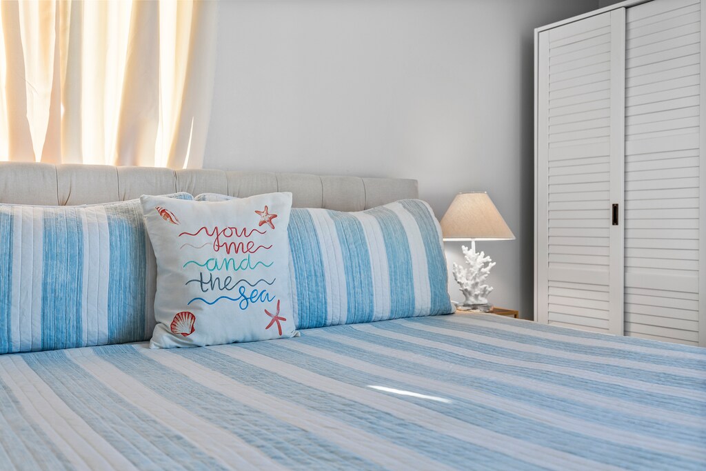 The simple and elegant decor, combined with natural light filtering through the curtains, creates a tranquil and inviting atmosphere, perfect for a peaceful escape by the sea.